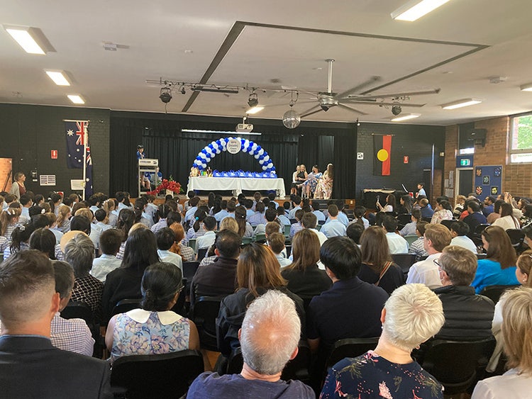 A wide shot of the school hall from behind the audience, looking towards the stage where awards are being presented.