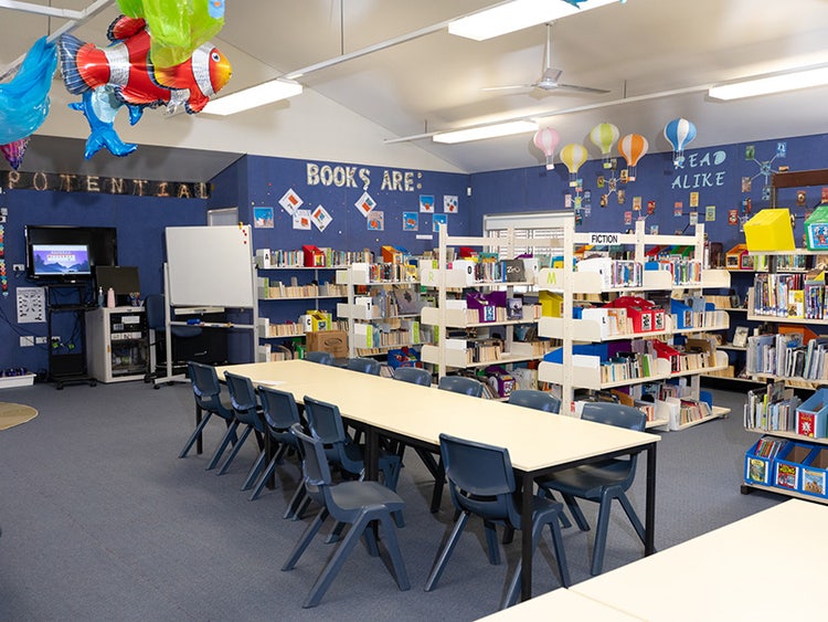 A wide shot of the school library interior including book shelves, table and chairs, and wall decorations.
