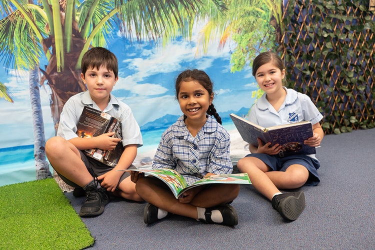 Three school children sitting on the floor with books in their laps.