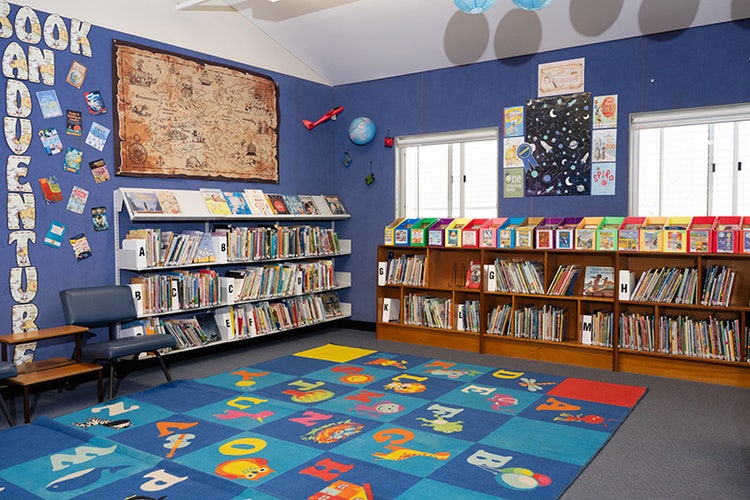 A section of a school library showing book shelves and a mat for children to sit on.