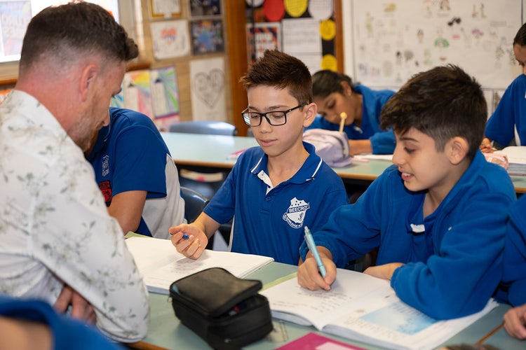 Two students facing one teacher, writing.